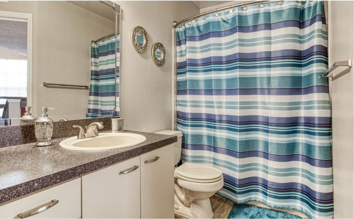 Bathroom with white cabinets, dark countertop, toilet, and blue striped shower curtain.
