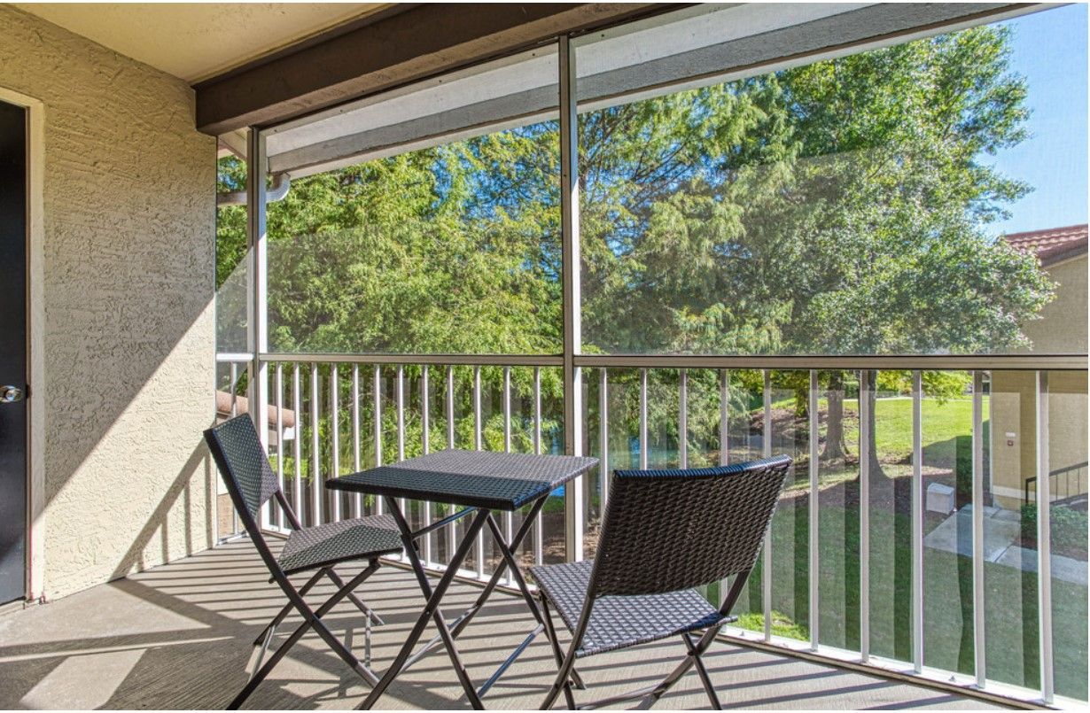 Balcony with small table and two chairs overlooking trees and water.