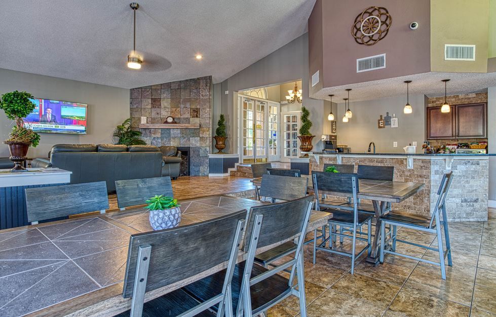 Lounge area with tables, chairs, sofa, fireplace, and kitchen area. Brown, gray, and neutral colors.