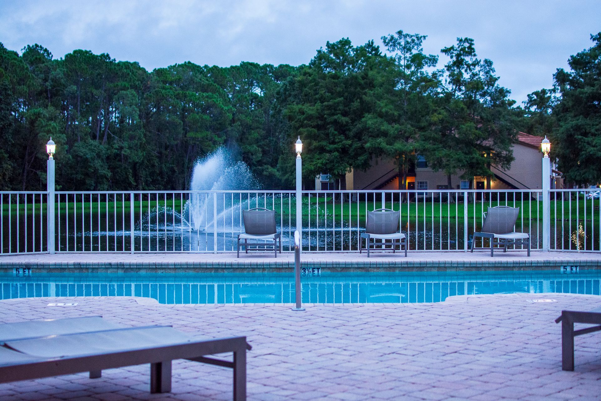 Poolside scene with chairs, fountain, and trees in background.