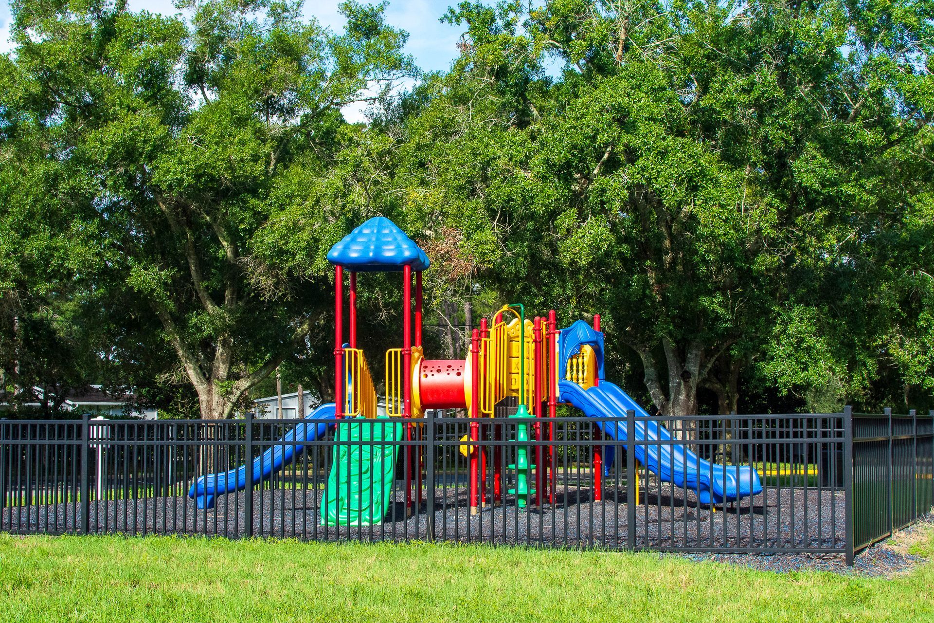 Colorful playground with slides, climbing structures, and a blue roof, enclosed by a black fence.