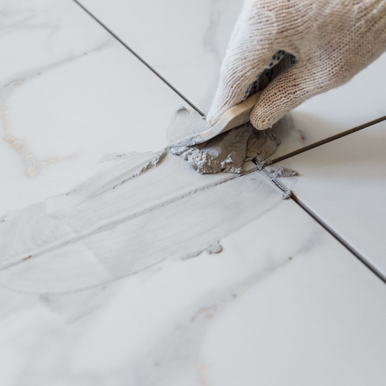 A person is applying grout to a tile floor with a spatula.