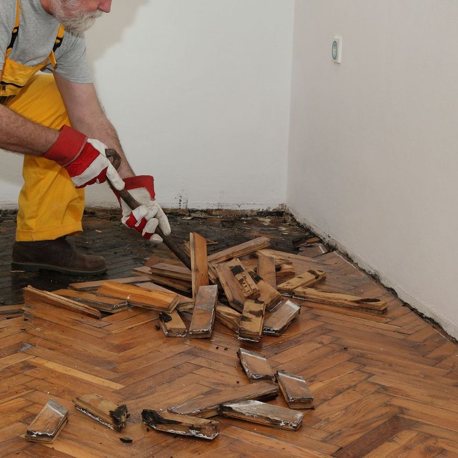 A man wearing yellow overalls and red gloves is breaking wood with a hammer