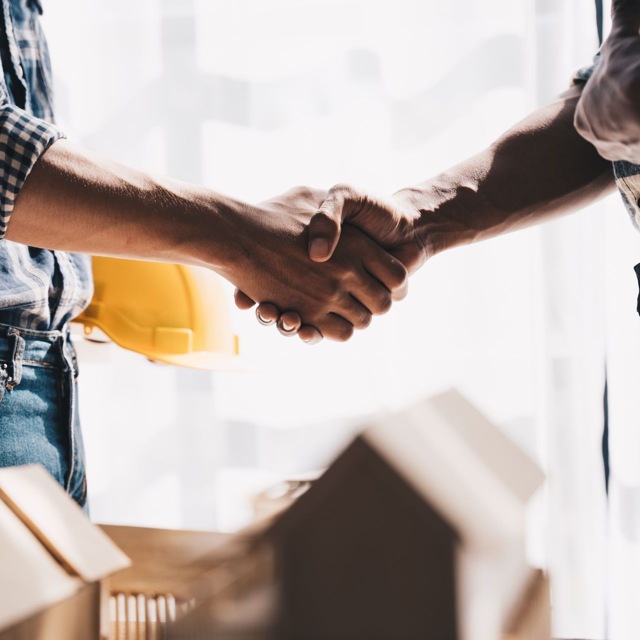 Two men are shaking hands in front of a model house.