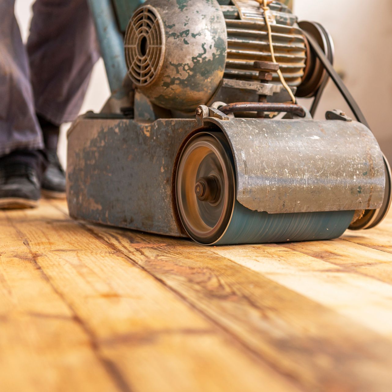 A person is sanding a wooden floor with a machine.