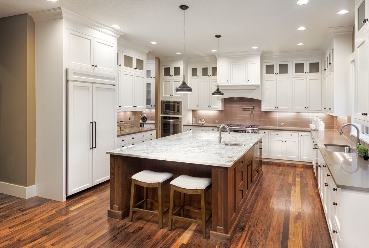 A kitchen with white cabinets and hardwood floors and a large island in the middle.