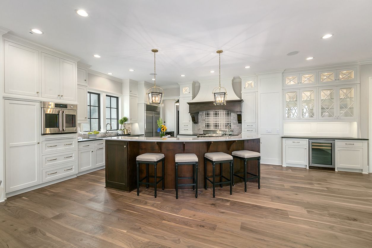 A kitchen with white cabinets , stainless steel appliances , hardwood floors and a large island.