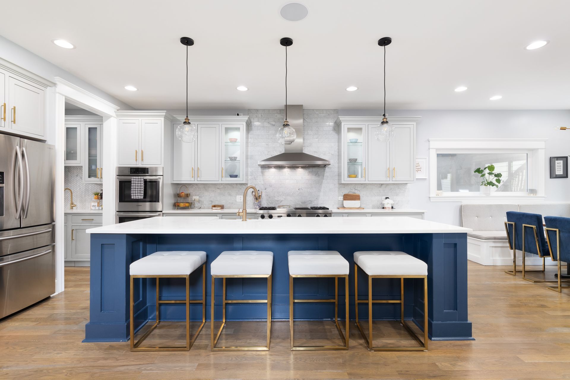 A kitchen with blue cabinets and white counter tops and stools.