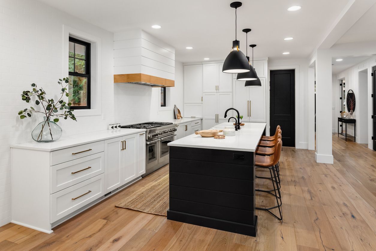 A kitchen with white cabinets , stainless steel appliances , hardwood floors and a black island.