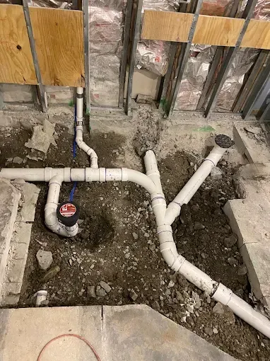 Plumbing pipes installed in the ground; PVC pipes and blue supply lines; construction site.