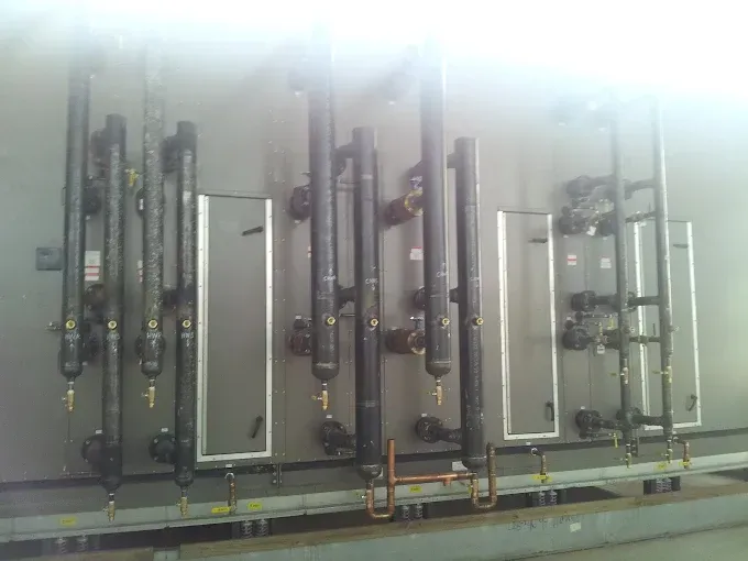 Black pipes and rectangular panels mounted on a wall. Copper piping and valves are also visible.