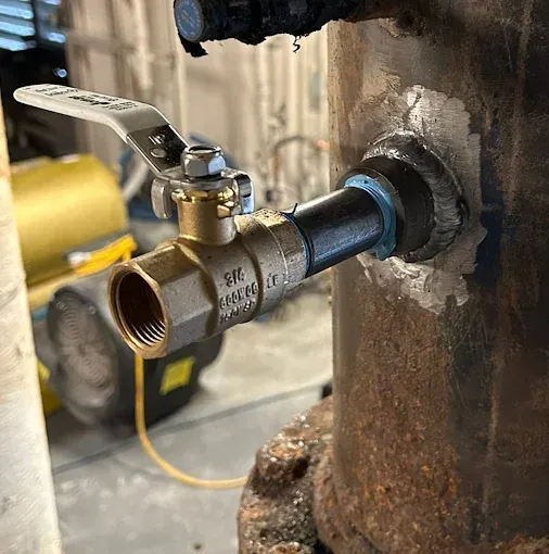 Bronze ball valve attached to a rusty metal pipe. Valve is open.