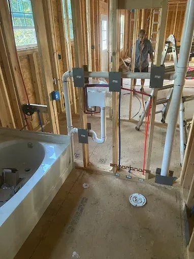 Bathroom under construction: wooden frame, plumbing fixtures, tub, and person working.