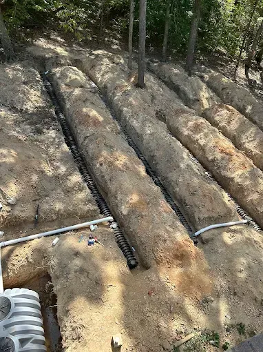 Trenches dug in soil, holding black drainage pipes, part of a septic system.
