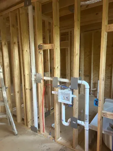 Interior wall with exposed plumbing and electrical wiring; construction site.