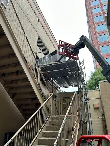 A lift raises equipment near a building's exterior stairwell, supported by scaffolding.