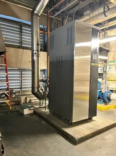 Industrial boiler with metal chimney and plumbing in a utility room.