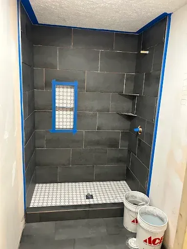 Newly tiled shower with gray walls, a mosaic floor, and built-in shelves.
