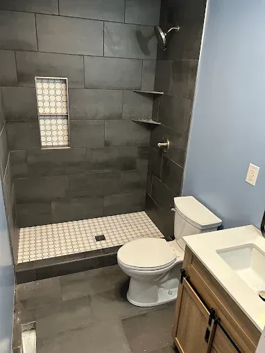 Bathroom with gray slate-tiled shower, white mosaic floor, toilet, vanity with wood cabinet, and light blue walls.