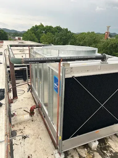 Rooftop HVAC unit with metal casing and black cooling grids. Piping extends from the unit.