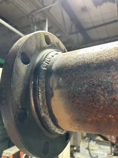 Flange welded to a rusted pipe, with a black flange and a weld seam.