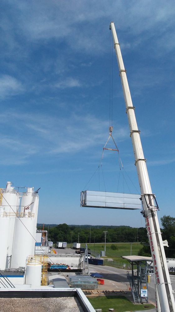 Crane lifting a rectangular container above an industrial site, blue sky background.