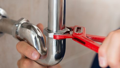 A plumber is fixing a pipe with a wrench.