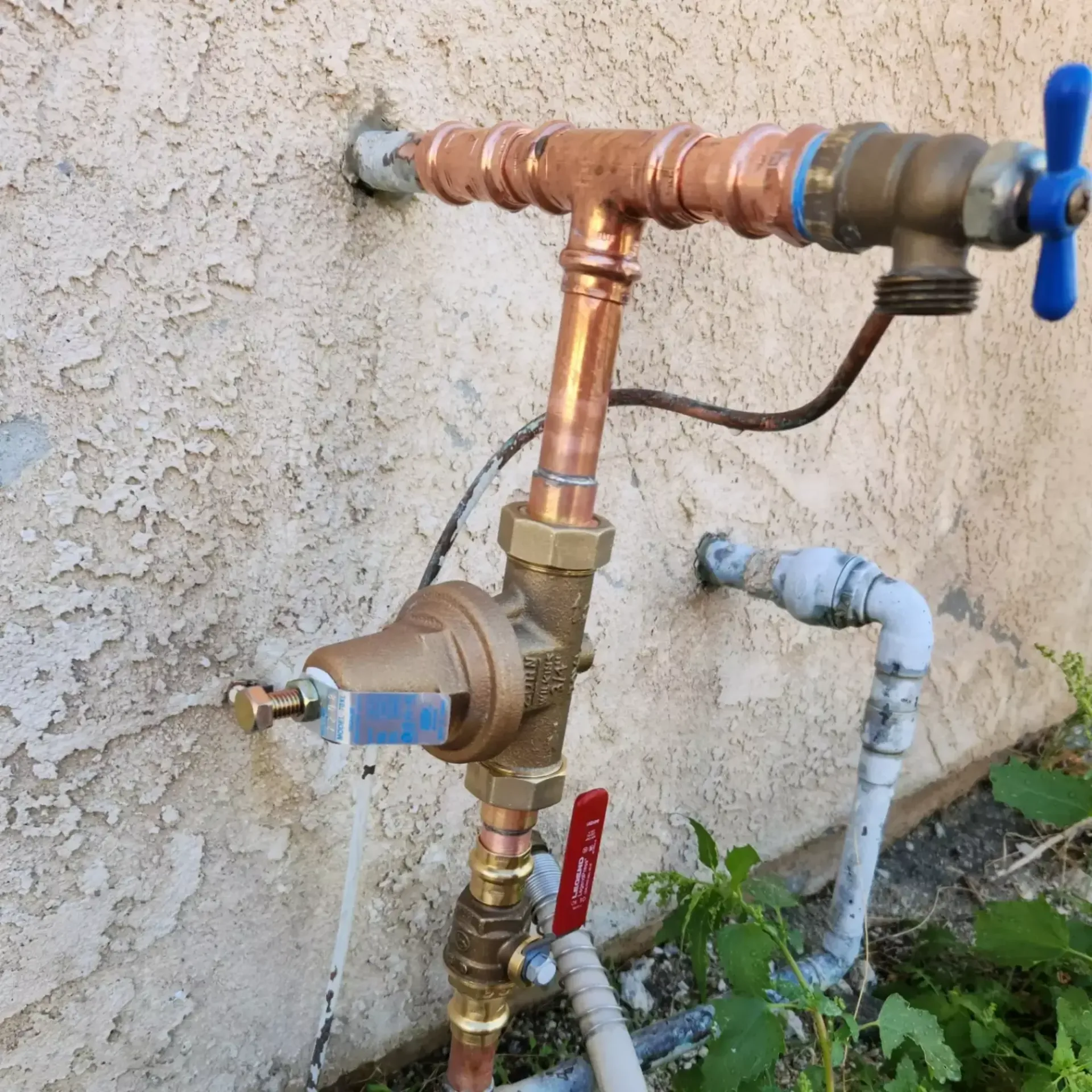 A copper pipe with a blue handle is attached to a wall