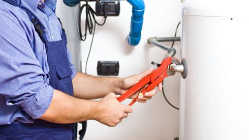 A plumber is fixing a water heater with a wrench.