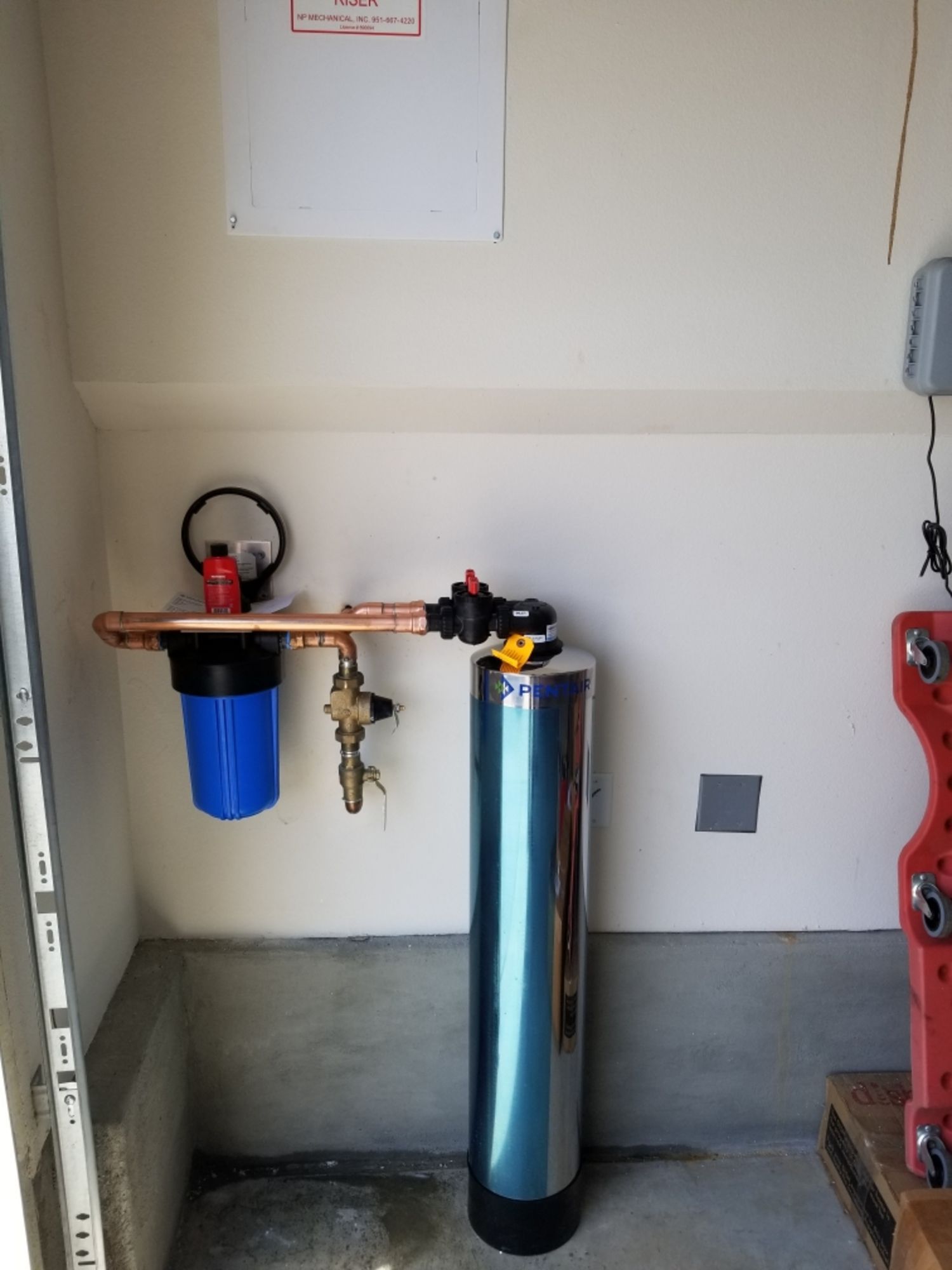 A stainless steel water filter is installed in a garage.