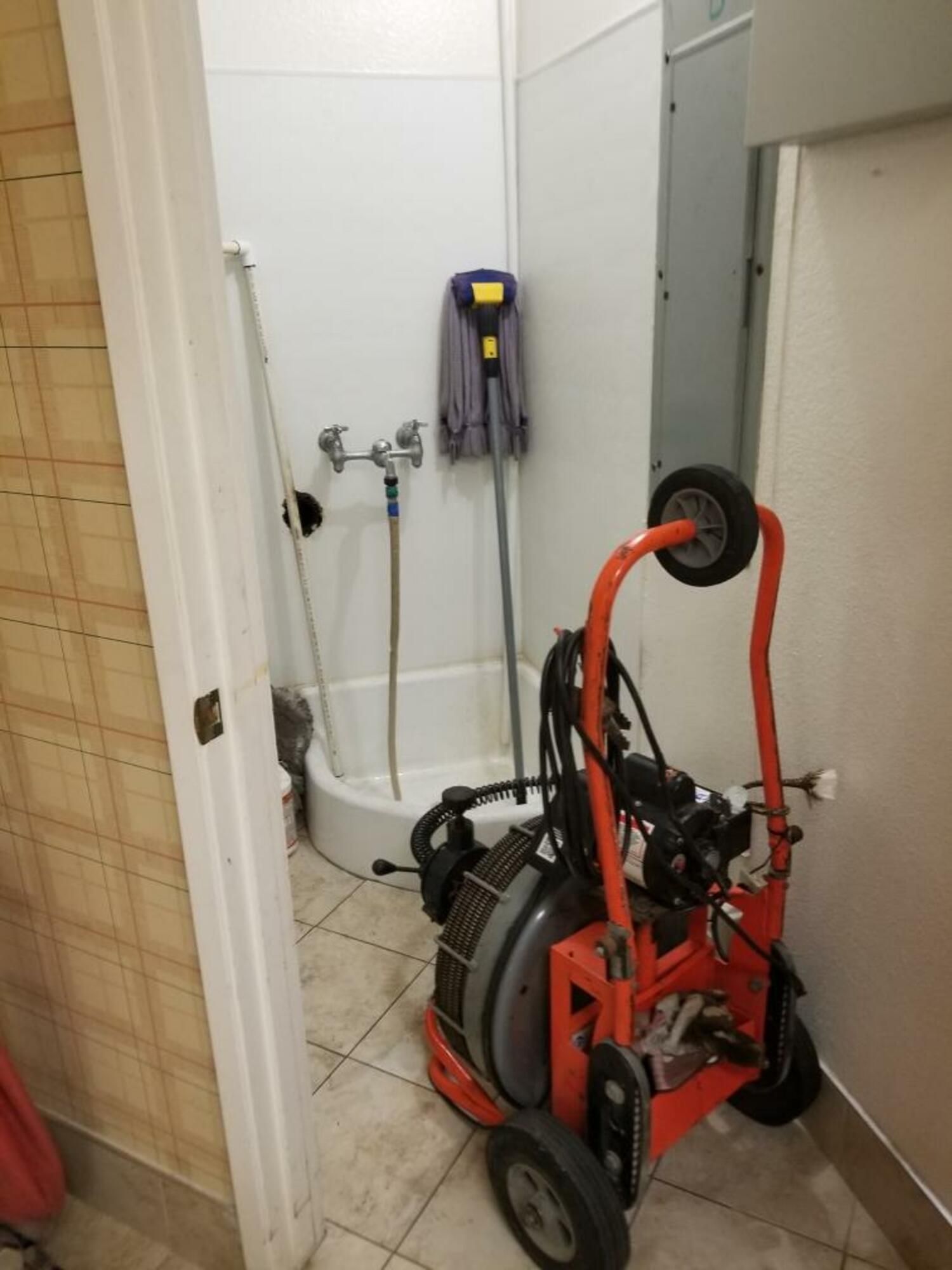 A drain cleaner is sitting in a bathroom next to a mop.