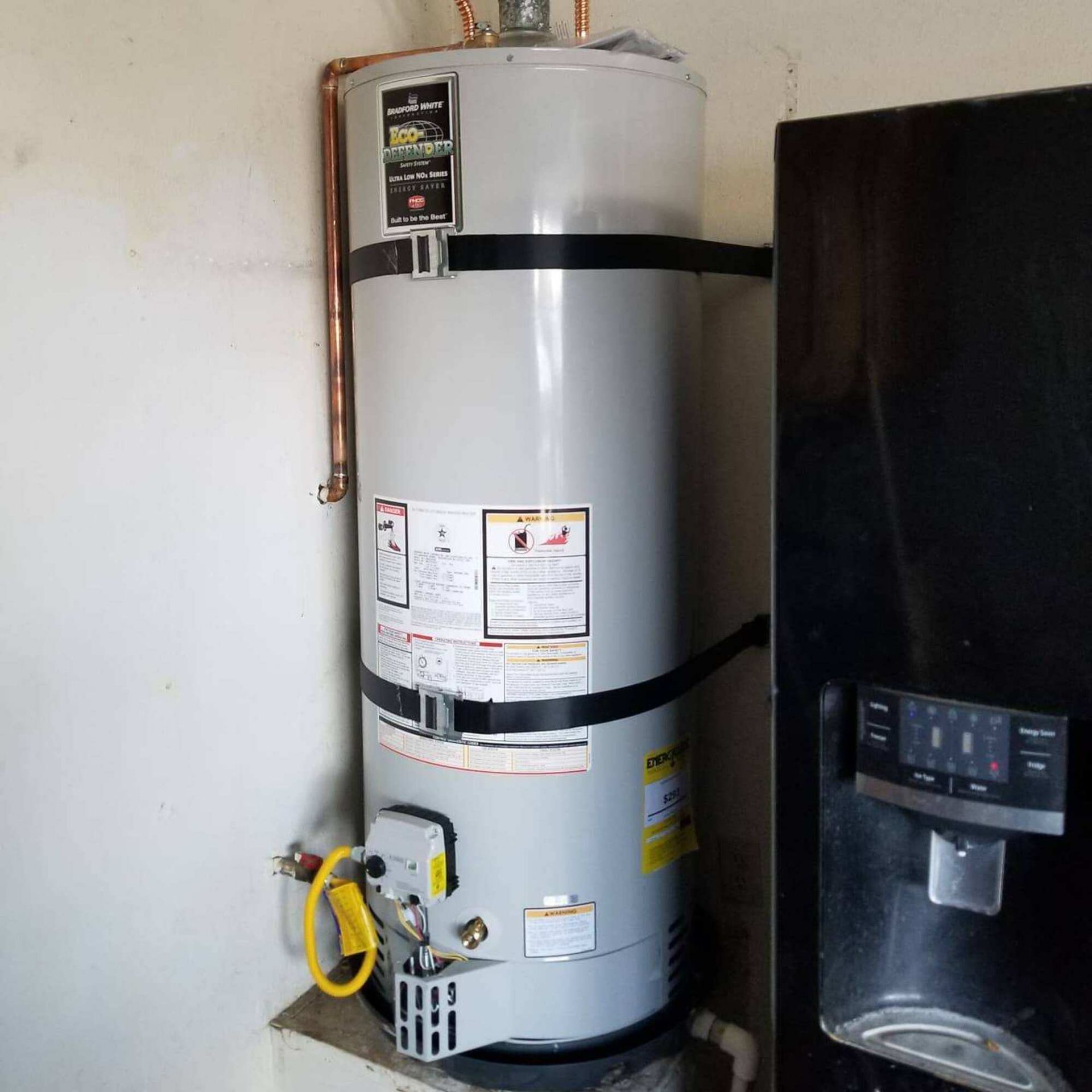 A water heater is sitting next to a refrigerator in a room.