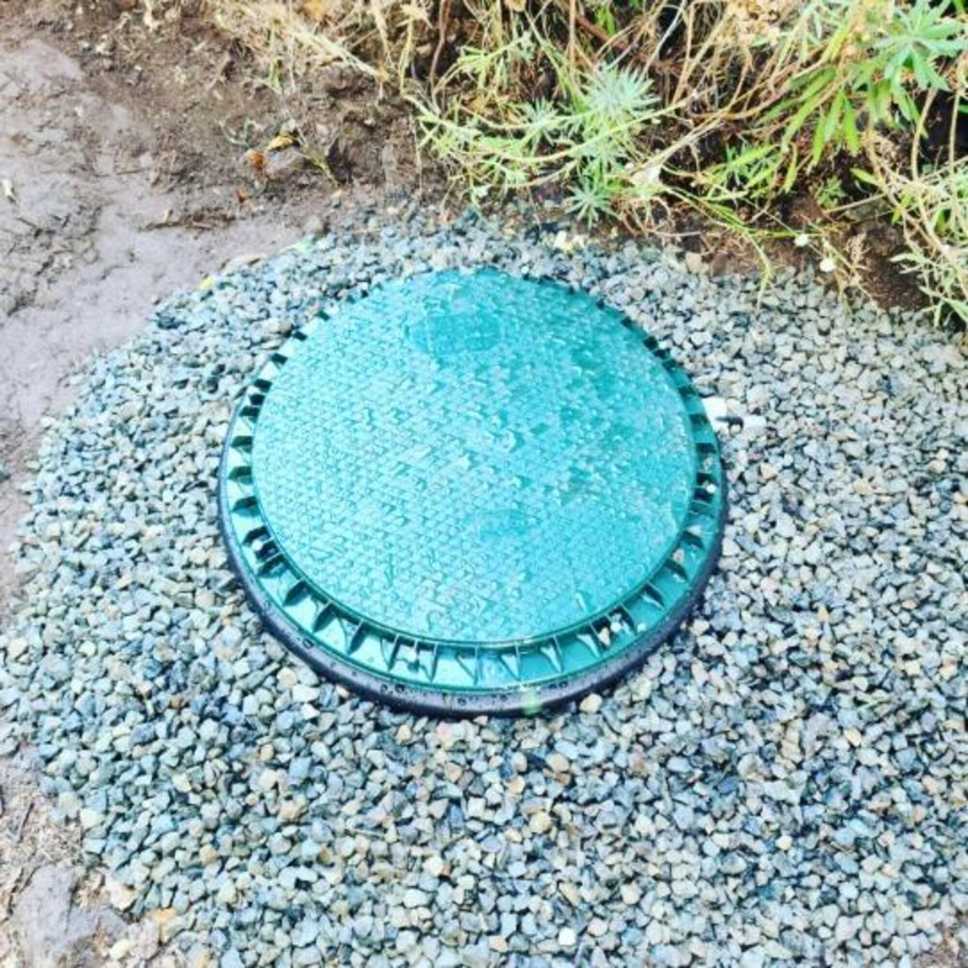 A green manhole cover is sitting on top of a pile of gravel.
