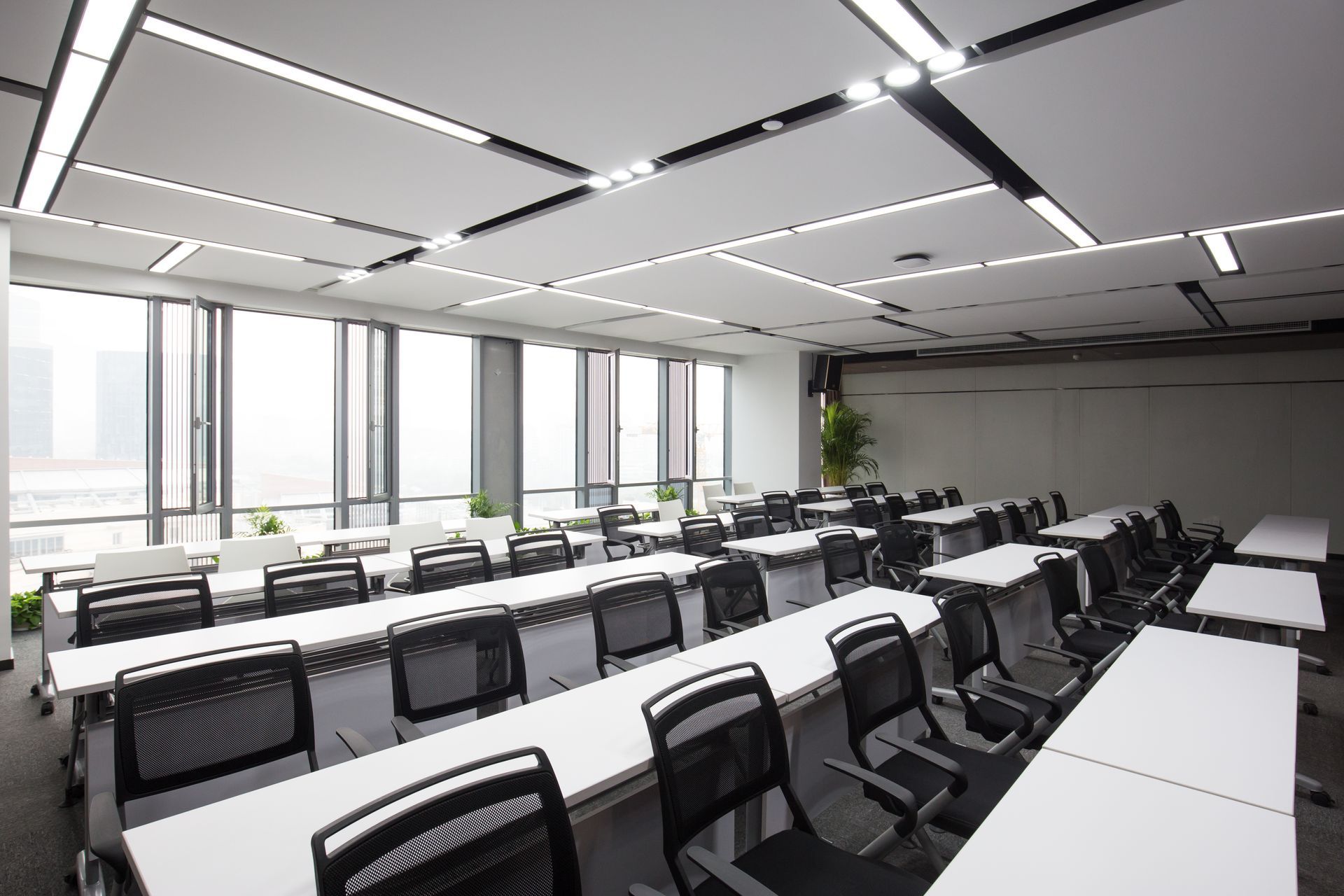 Empty modern classroom with rows of desks, chairs, and large windows.