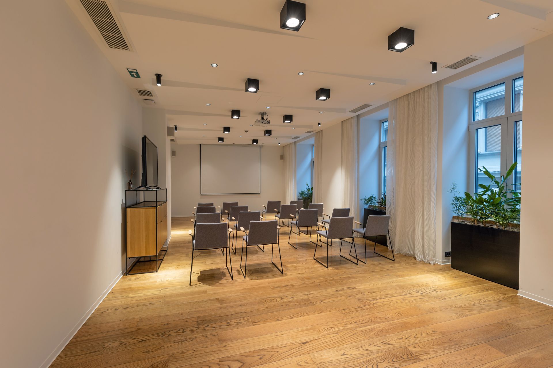 Conference room with chairs facing a screen, light wood floor, and white walls.