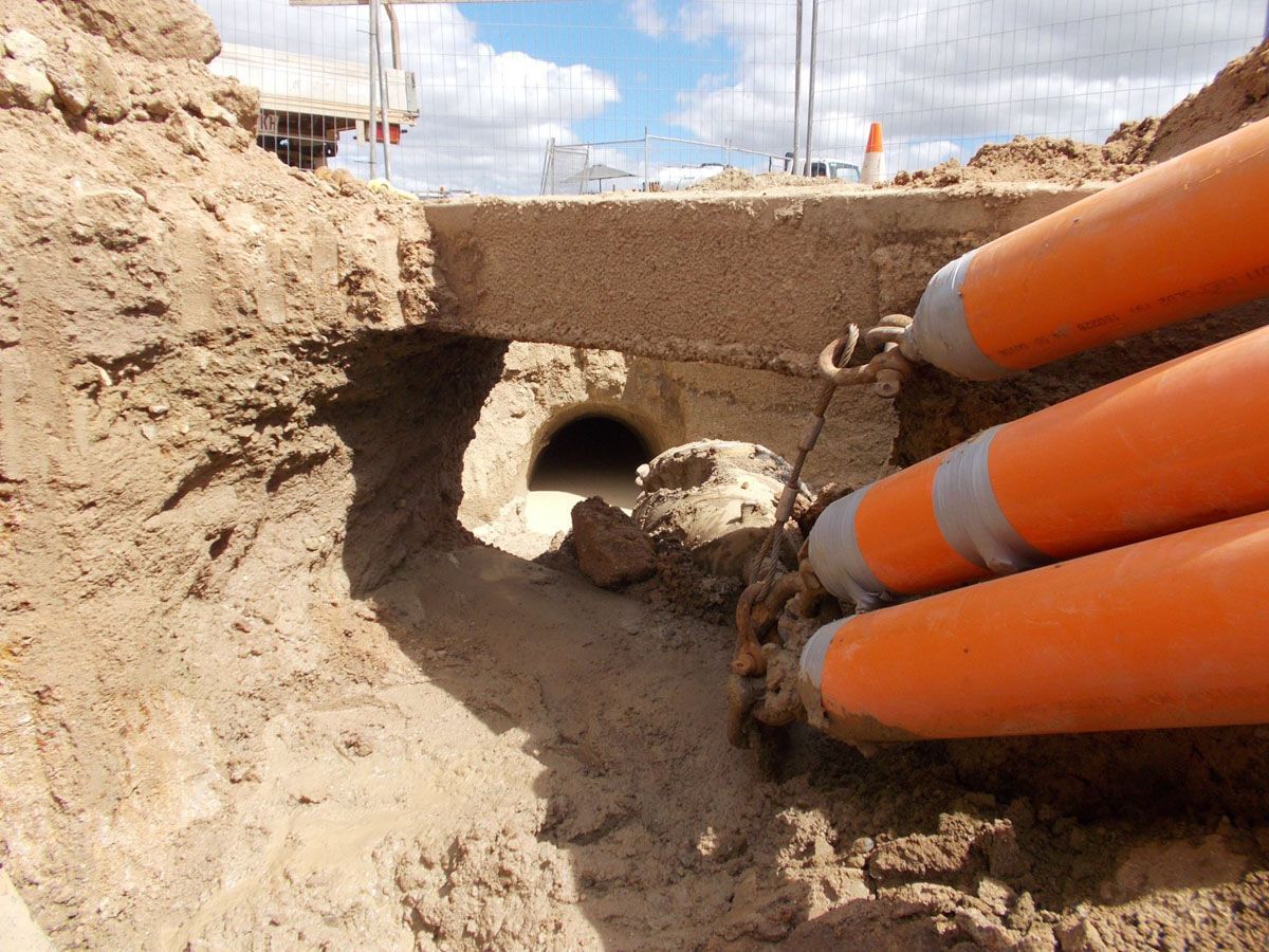 A man wearing a hard hat and headphones is standing on a construction site holding a hose.