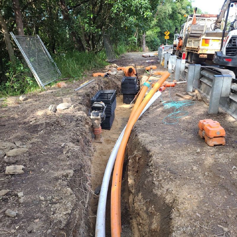 A bunch of pipes are laying in the dirt on the side of a road.
