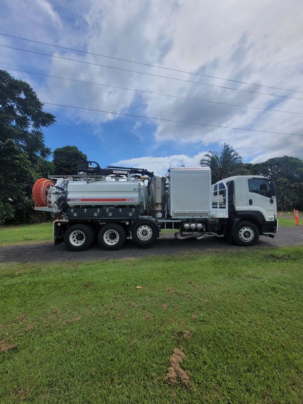A white vacuum truck is parked in a grassy field.