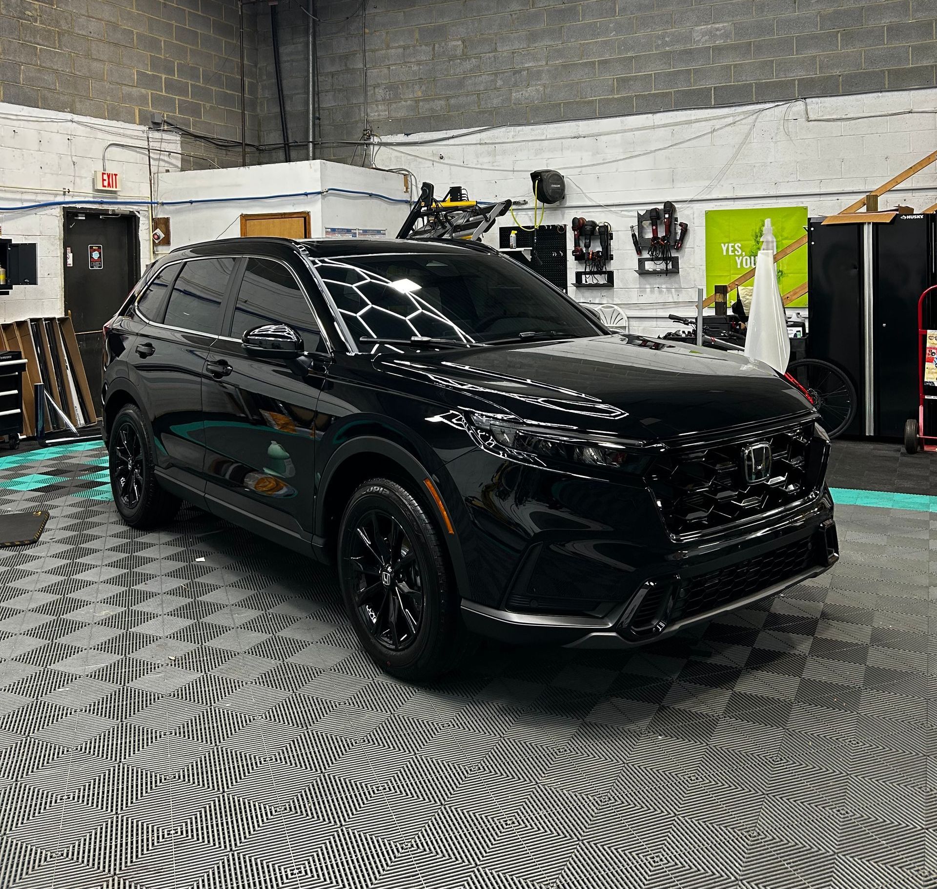 A black car is parked in a garage under a honeycomb light.