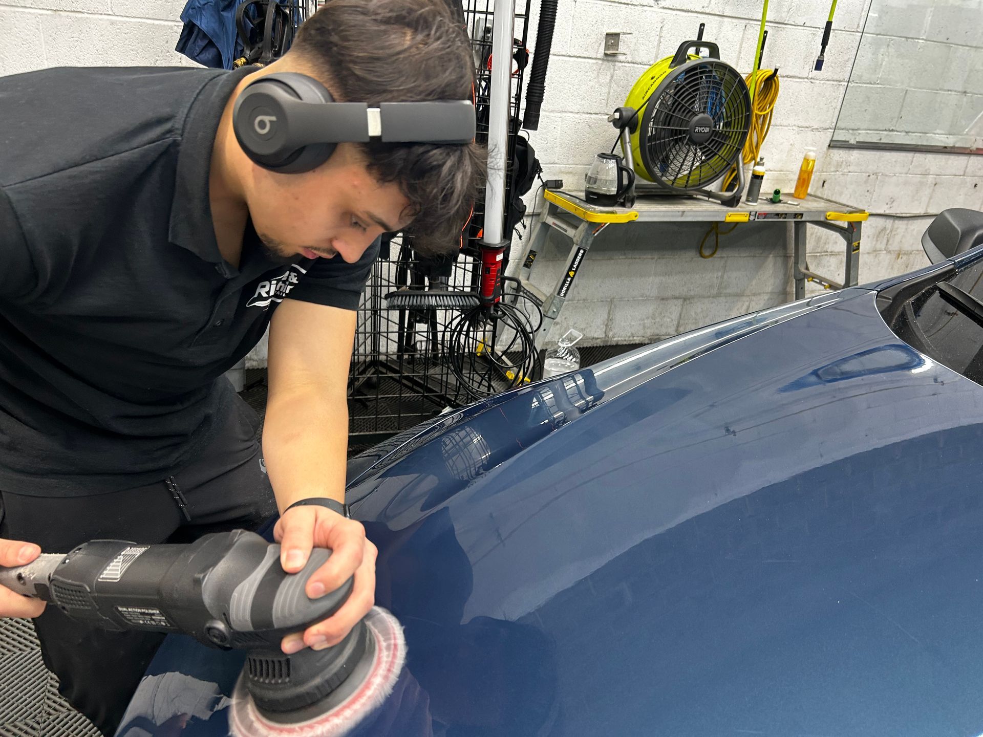 A man wearing headphones is polishing the hood of a car.
