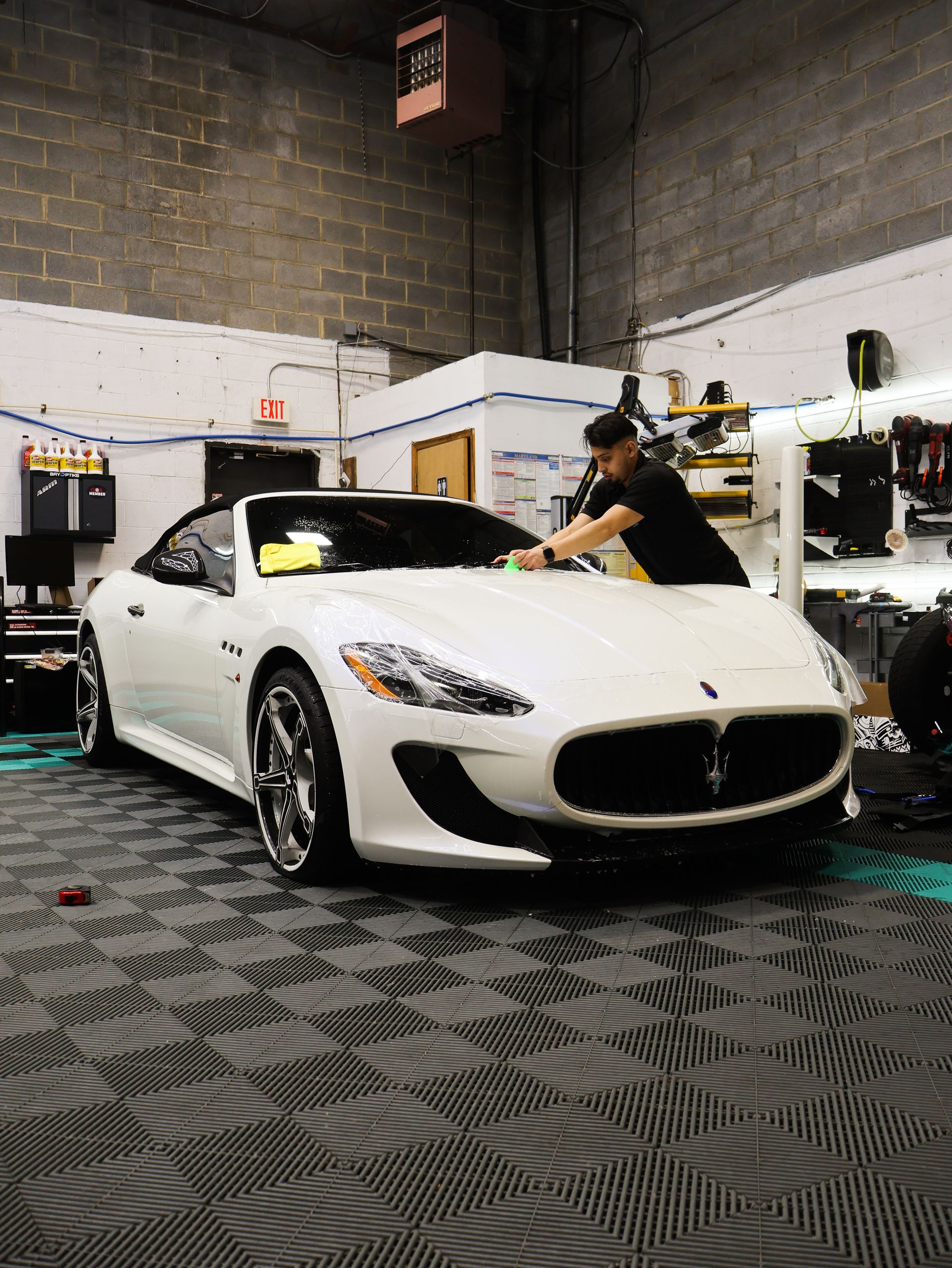 A man is cleaning a white maserati car in a garage.