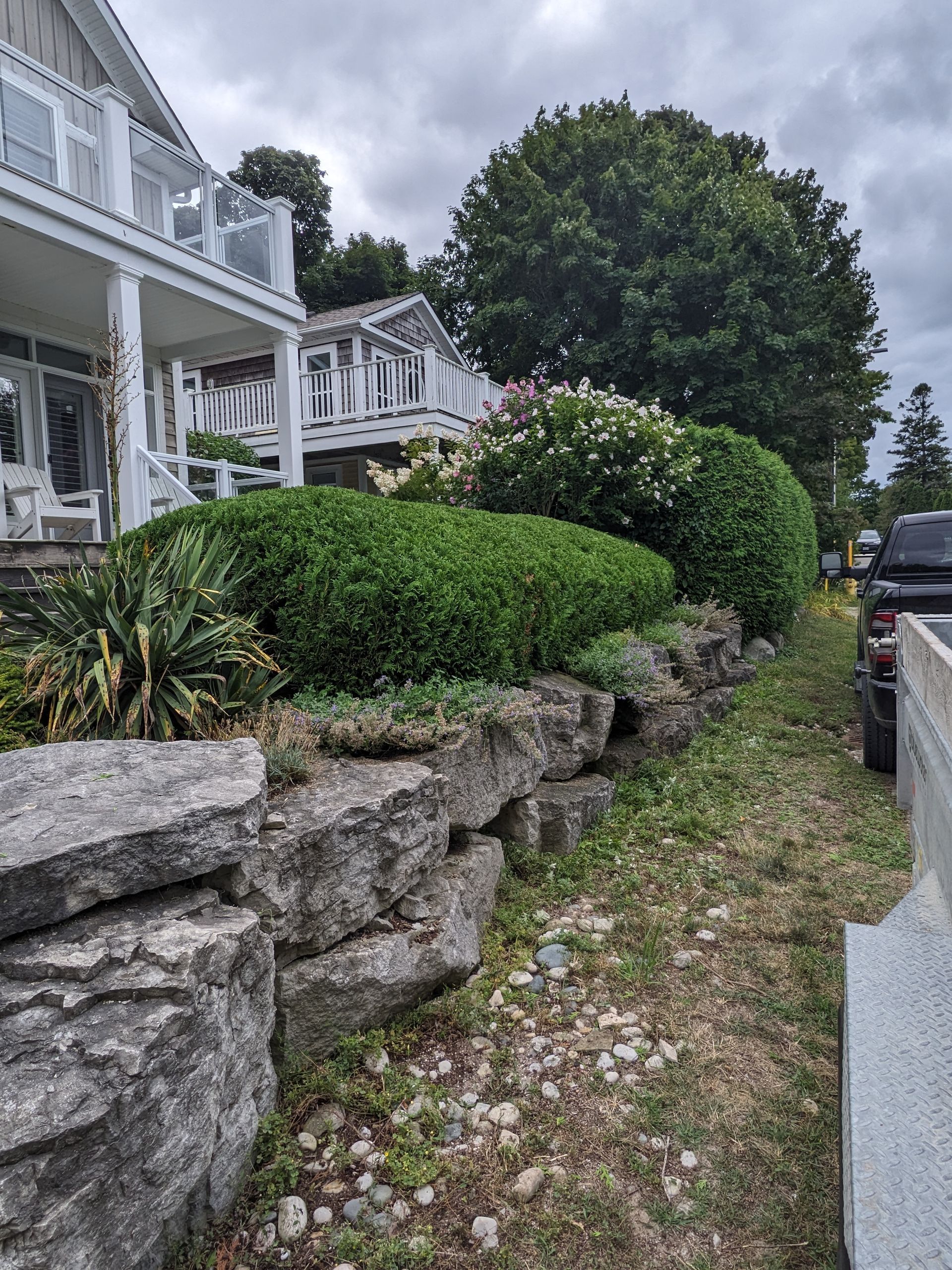 A large house with a stone wall and bushes in front of it.