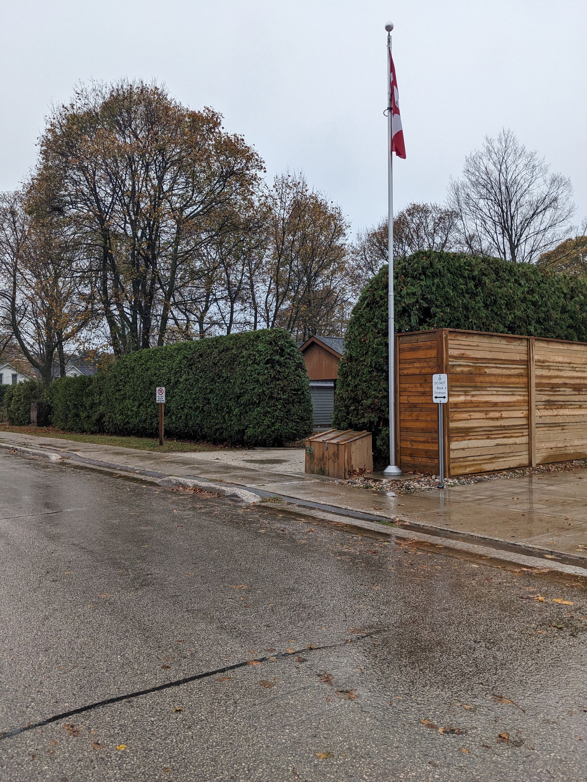 A canadian flag is flying on a pole in front of a wooden fence.