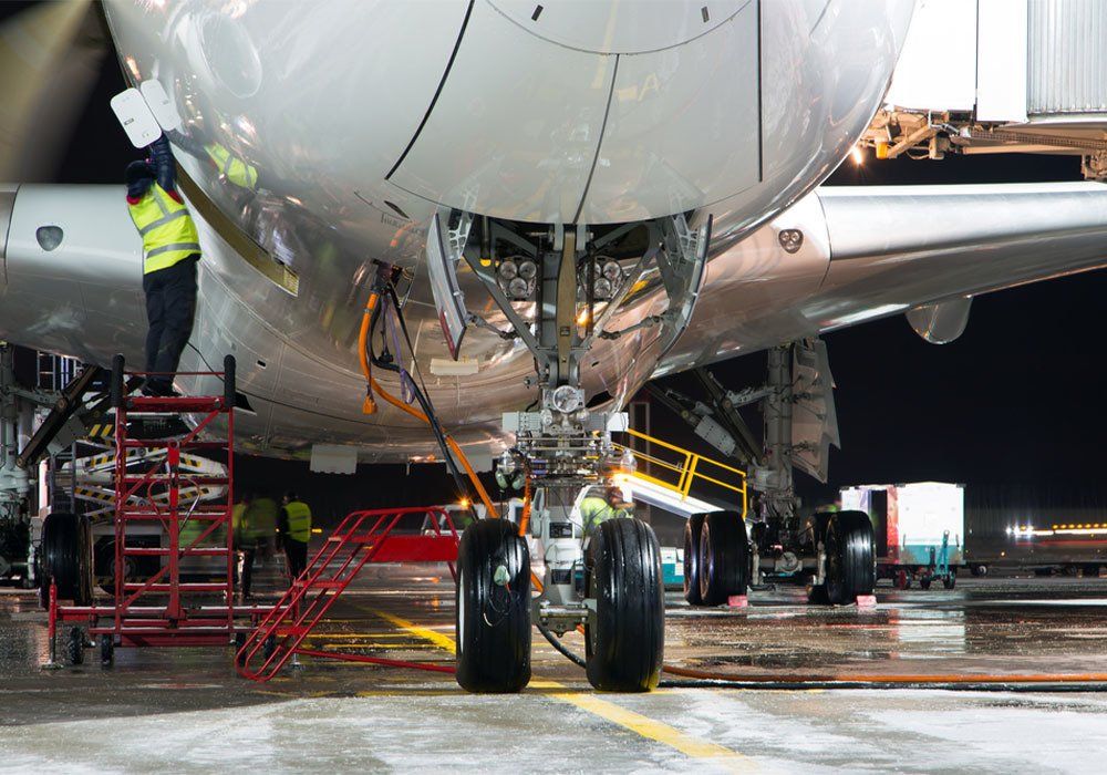 Pre-flight service of modern passenger aircraft in the night airport. The main landing gear close up. The plane is parked on the airport apron. - Image
