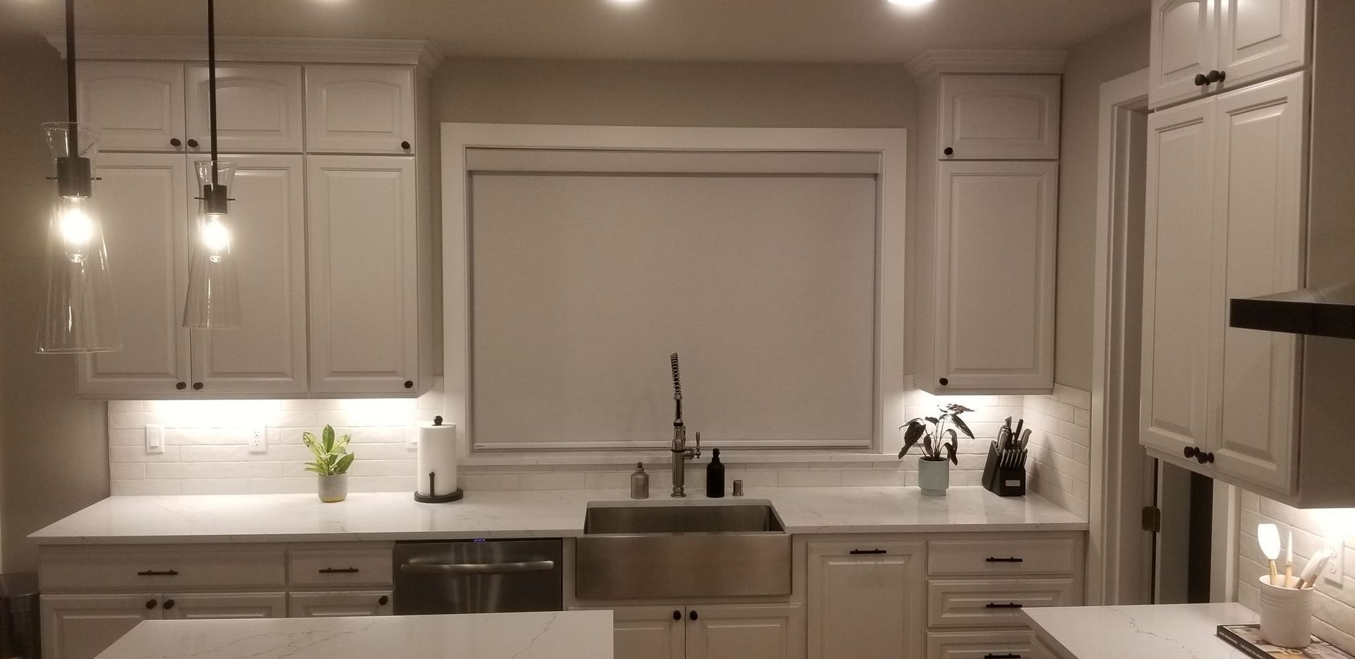 A kitchen with white cabinets, light countertops, a stainless steel apron-front sink, and two pendant lights.