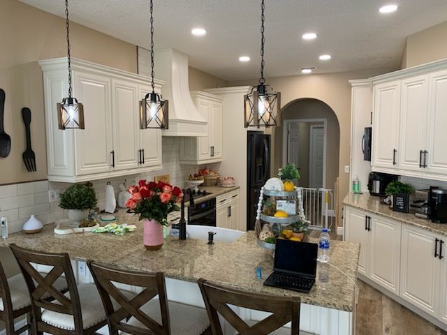 A bright kitchen with white cabinets, granite countertops, three hanging pendant lights, and a bouquet of roses.