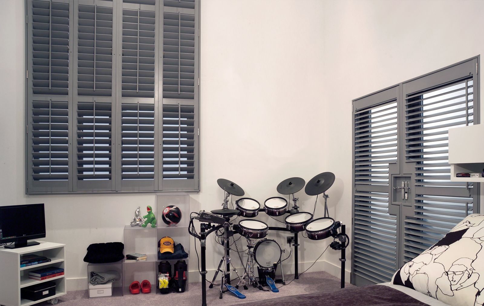 A bedroom featuring a gray electronic drum kit, shutters on windows, a small storage unit, and a television.