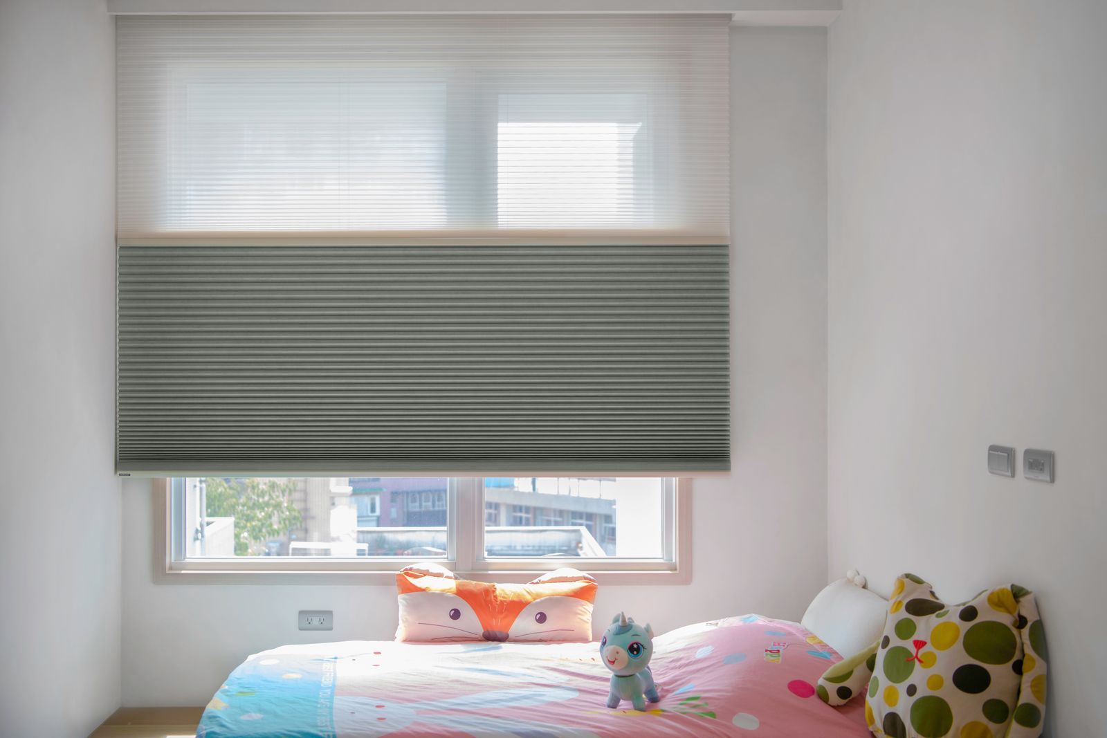 A bedroom featuring a window with dual-layer shades, a pink bed, a fox-shaped pillow, and a plush toy.