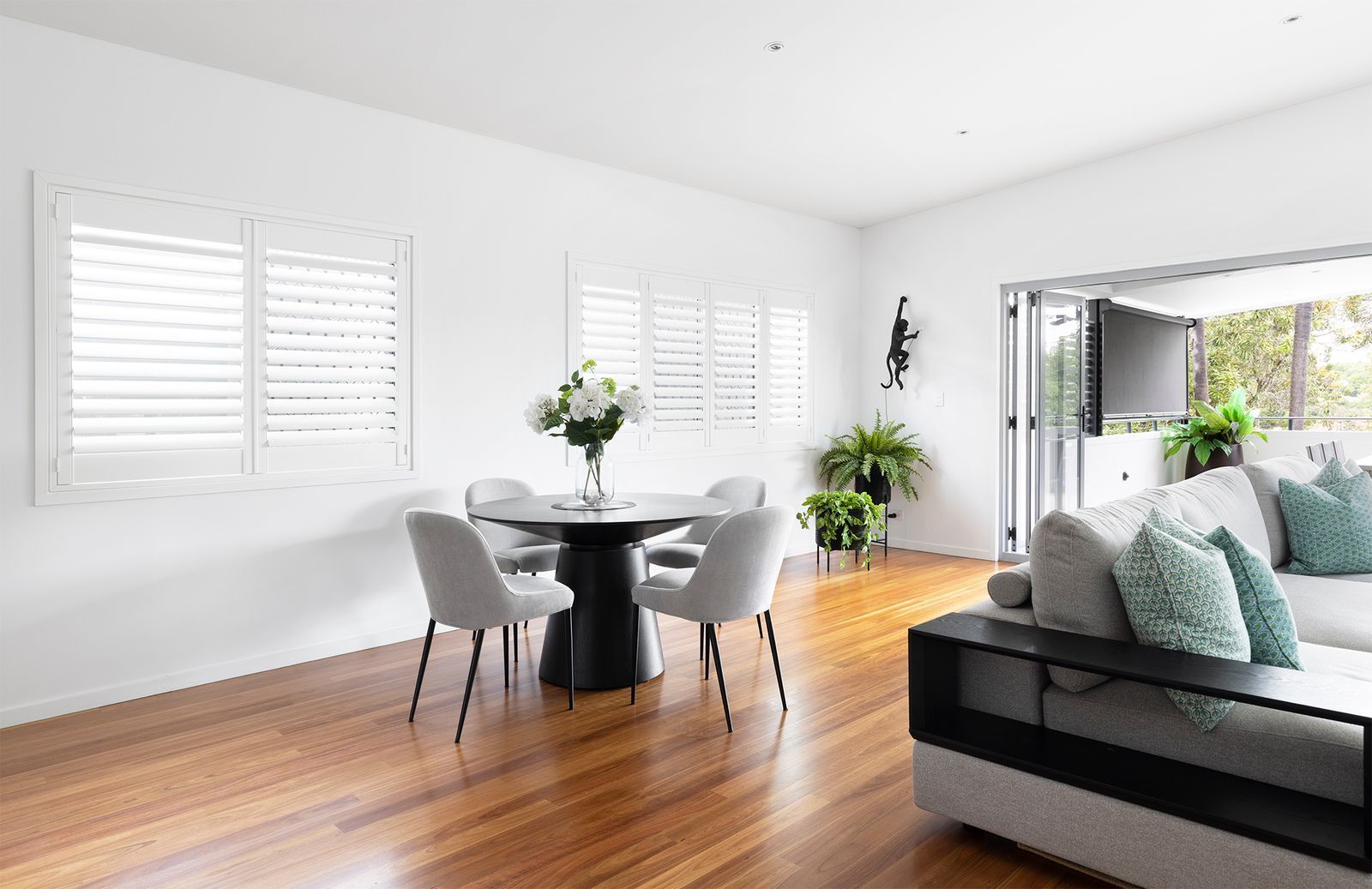 A modern, bright living and dining room with a round table, white chairs, wooden floors, and a grey sectional sofa.