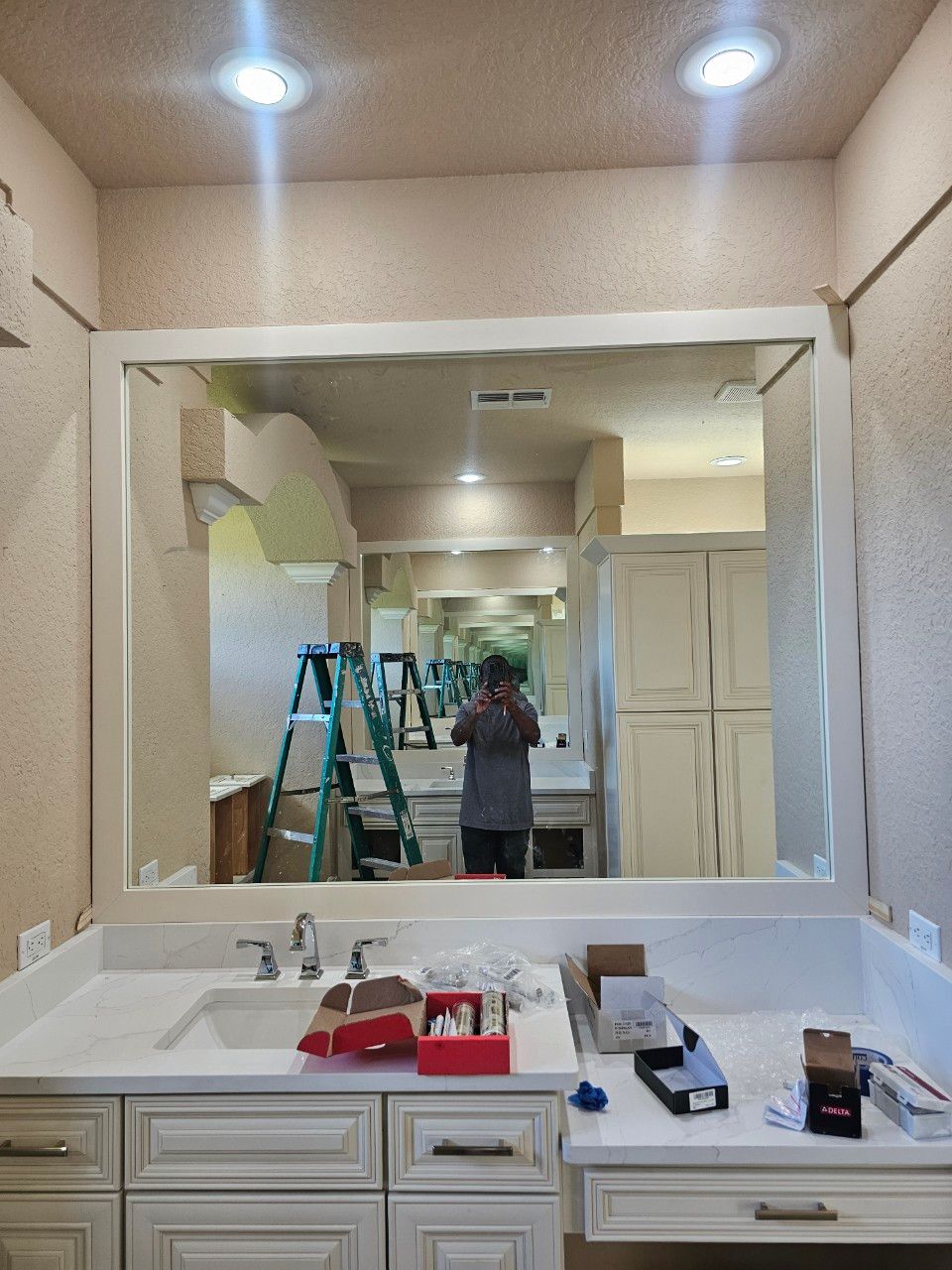 Bathroom vanity with white cabinets, a stone countertop, a large framed mirror, and two overhead recessed lights.